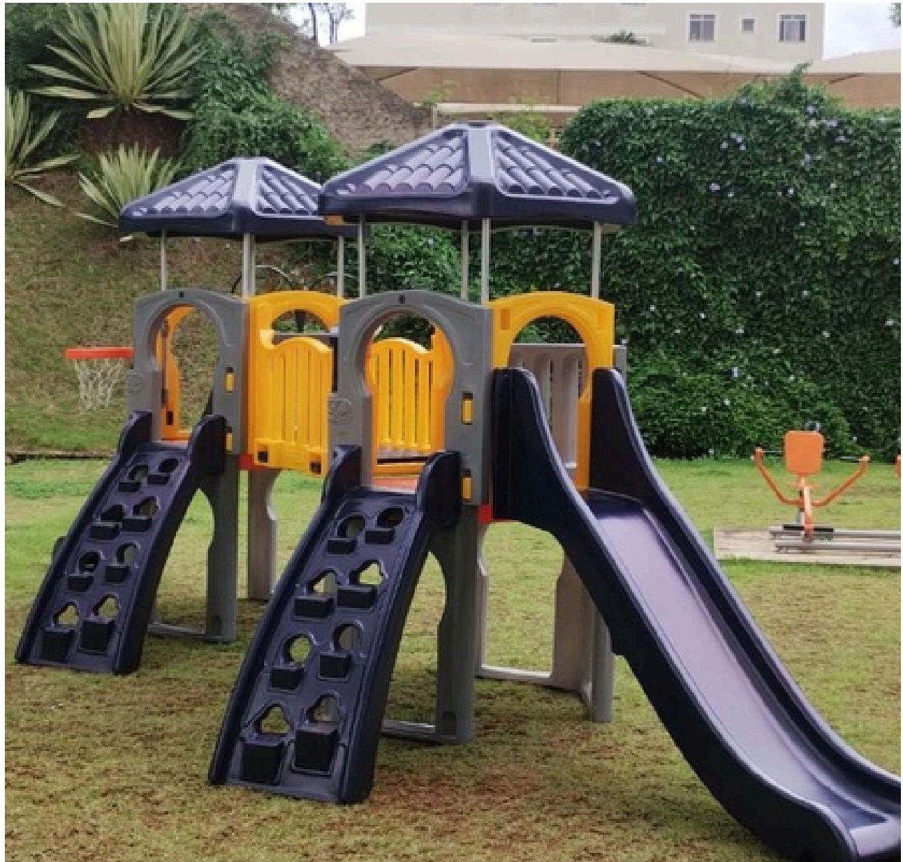 Playground de madeira plástica com duas torres, paredes de escalada e escorregadores instalado em área comum